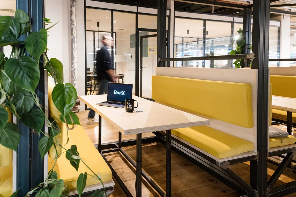 Espace de pause des bureaux de Brut à Paris — banquettes jaunes, ordinateur affichant BrutX et mug Ici c'est Brut