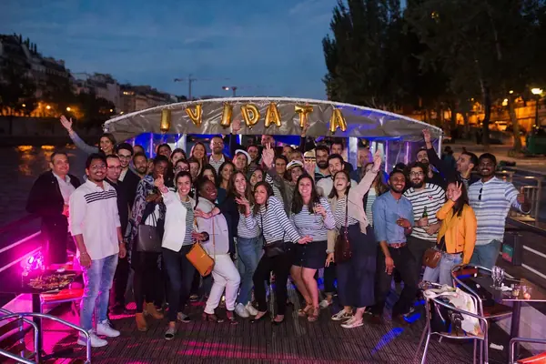 Photo de groupe d'une équipe d'entreprise sur le pont d'un bateau sur la Seine à la tombée de la nuit, ballons dorés formant le nom de la société