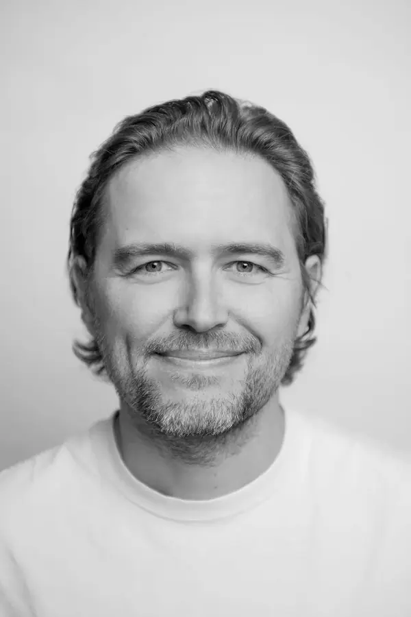 Portrait professionnel en noir et blanc d'un homme souriant en t-shirt blanc sur fond clair, séance pour AKRONE