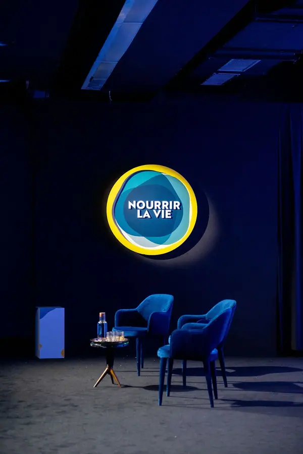 Scène sombre avec fauteuils bleus et logo lumineux Nourrir la vie, reportage photo événementiel groupe Avril
