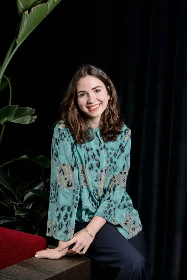 Portrait corporate d'une femme souriante en chemisier imprimé, assise dans un intérieur sombre