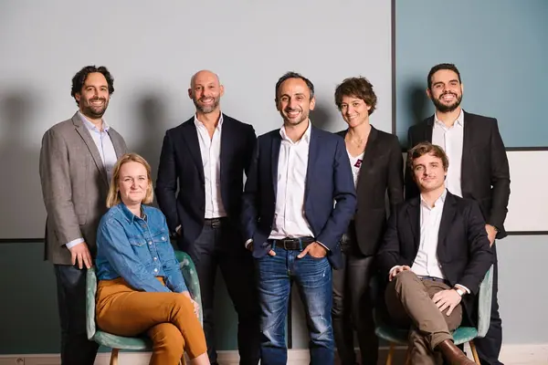 Photo d'équipe de 2CFinance, collaborateurs debout et assis devant un mur gris et vert, portrait corporate collectif