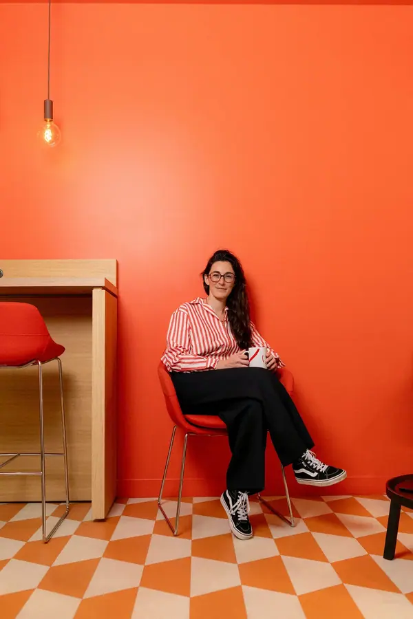 Portrait professionnel de Bénédicte assise dans un fauteuil œuf, livre en main, devant une bibliothèque aux tons chaleureux