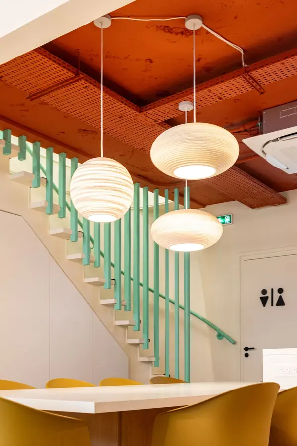 Espace de réunion des bureaux France Défi : plafond terracotta, suspensions en papier et chaises moutarde autour d'une table