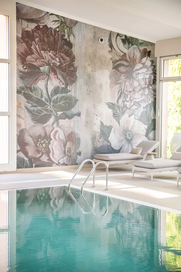 Piscine intérieure du spa du Domaine de la Gracieuse devant un grand papier peint floral, lumière naturelle