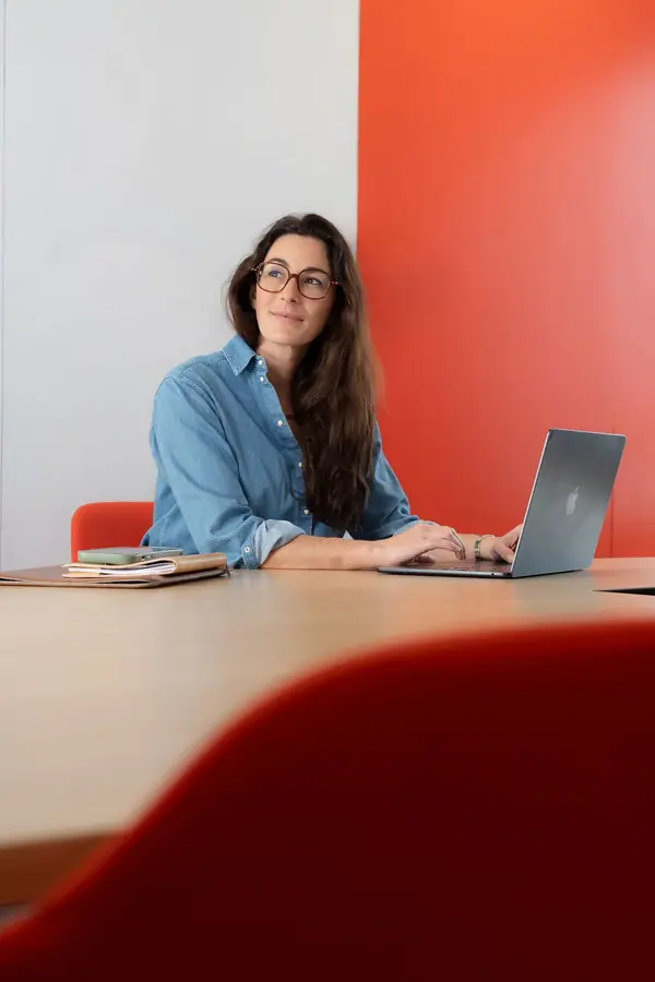 Portrait corporate d'une femme assise à une table de réunion devant un mur rouge, dans les locaux de son entreprise