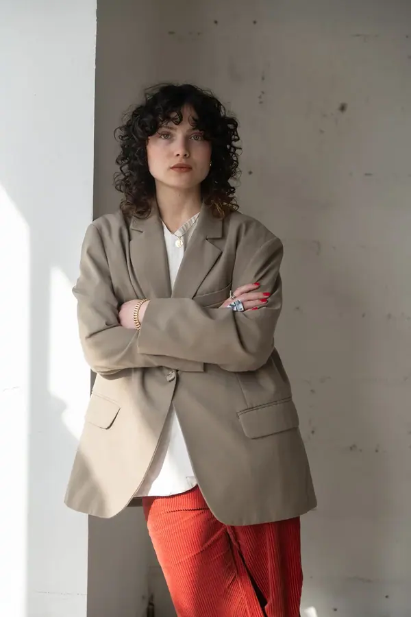 Portrait professionnel d'une architecte en blazer beige, bras croisés contre un mur blanc éclairé par la lumière naturelle