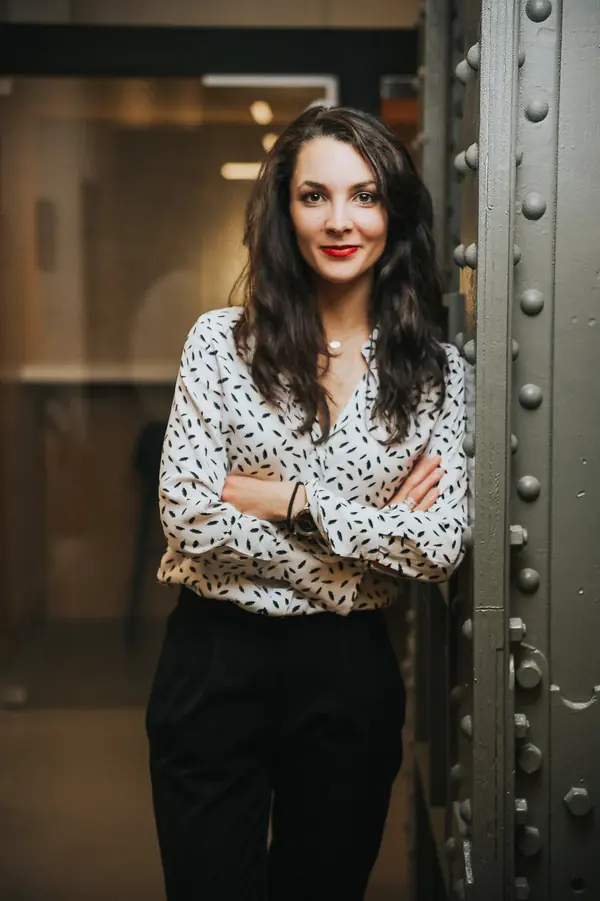 Portrait corporate d'une collaboratrice d'Affinion, bras croisés, adossée à une poutre métallique rivetée