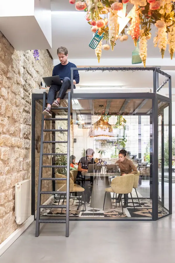 Mezzanine métallique avec échelle et bureau vitré sous un lustre fleuri, photographie d'architecture intérieure Yemanja