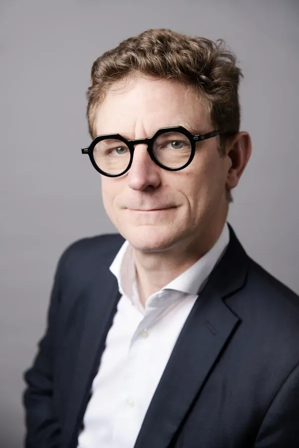 Portrait studio du dirigeant de Keobiz, lunettes rondes et veste marine sur fond gris