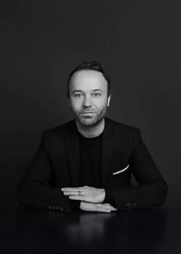 Portrait corporate noir et blanc de Sylvain, directeur de la communication, mains jointes sur une table, fond sombre