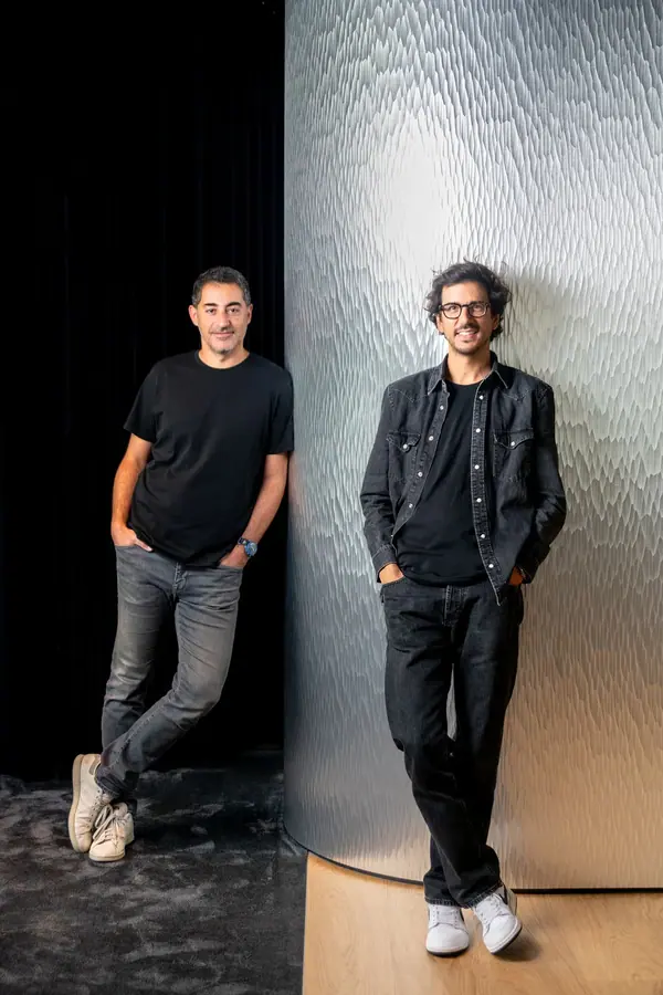 Portrait corporate de deux associés d'un fonds d'investissement appuyés contre une paroi métallique ondulée, fond sombre