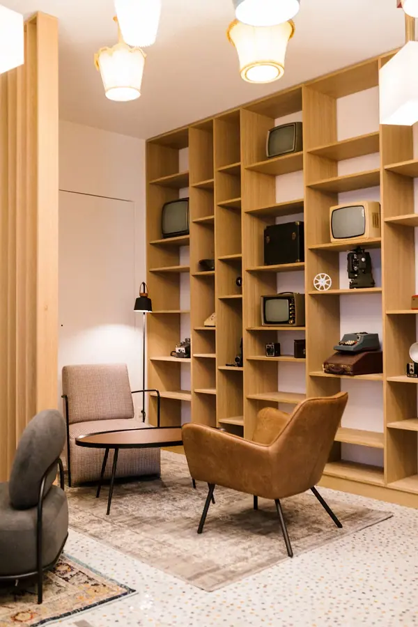 Salon du siège Mediawan à Paris, fauteuils en cuir et bibliothèque en bois garnie de téléviseurs vintage, lumière chaude