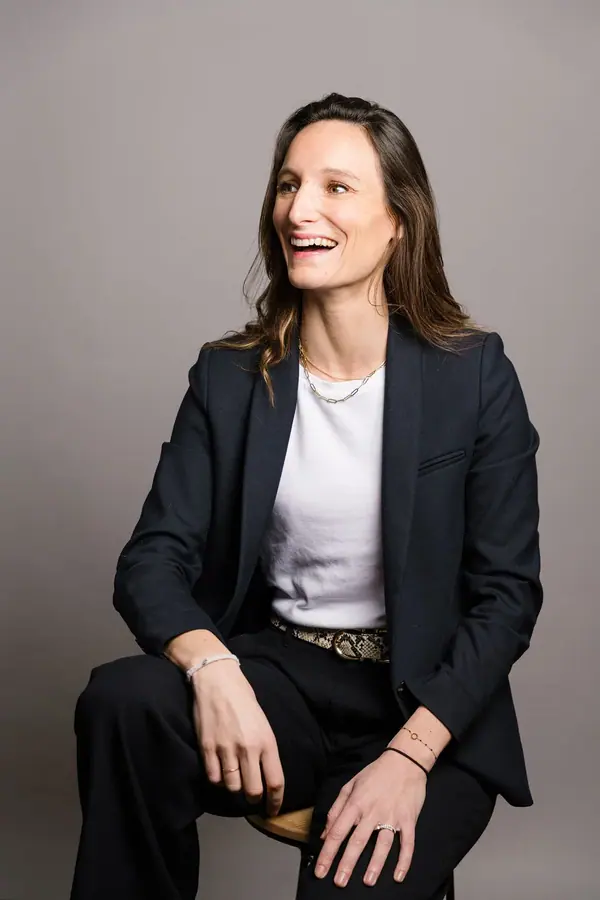 Portrait corporate d'une consultante de 2CFinance en blazer marine, assise sur un tabouret devant un fond gris