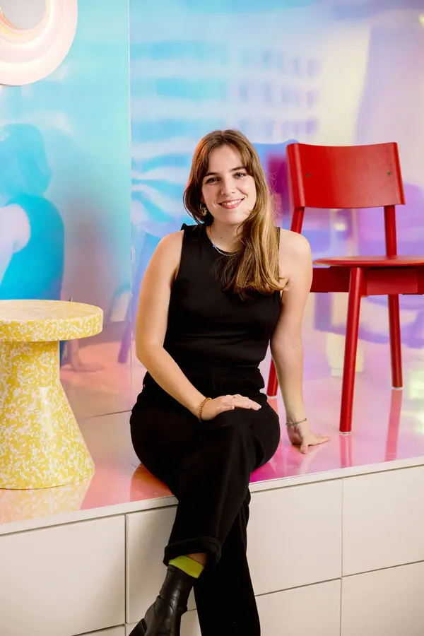 Portrait corporate d'une femme en noir assise devant un décor coloré et une chaise rouge, cabinet d'architectes