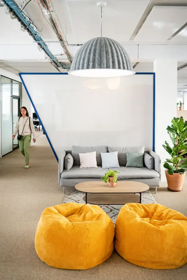 Bureaux Hublo à Paris : cloison triangulaire blanche bordée de bleu, canapé gris et poufs jaunes, photographie d'intérieur