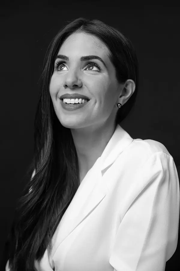 Portrait professionnel en noir et blanc de Marine, parfumeuse, souriante en veste blanche sur fond noir
