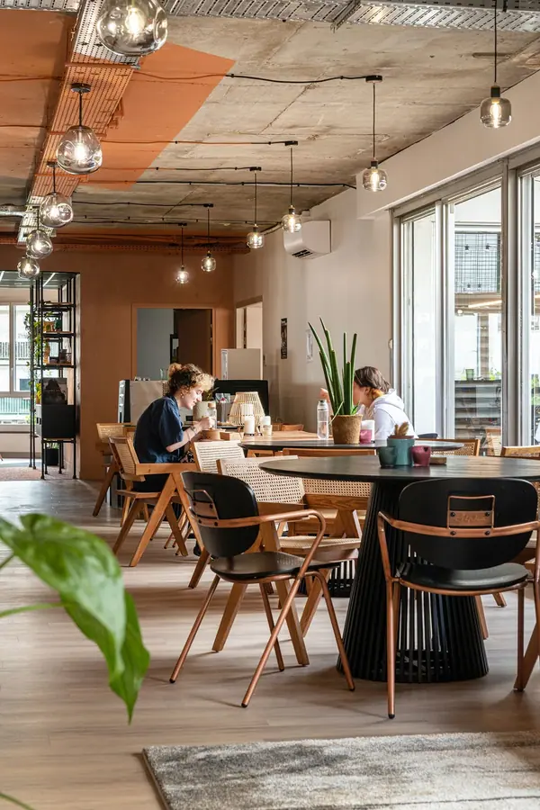 Espace de travail ouvert des bureaux Sloclap à Paris, plafond béton brut, tables en bois et chaises cannées sous la lumière