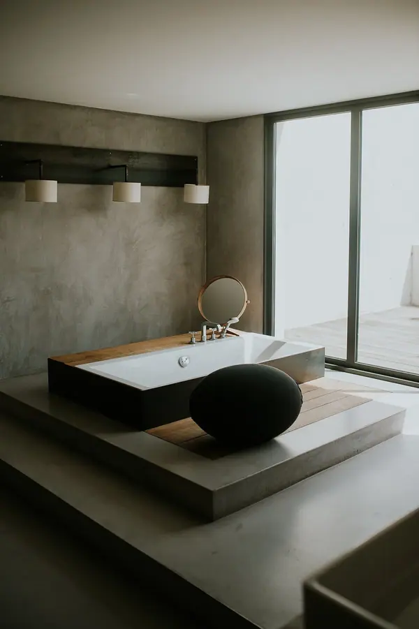 Baignoire îlot sur estrade en béton près d'une baie vitrée, photographie d'architecture intérieure contemporaine