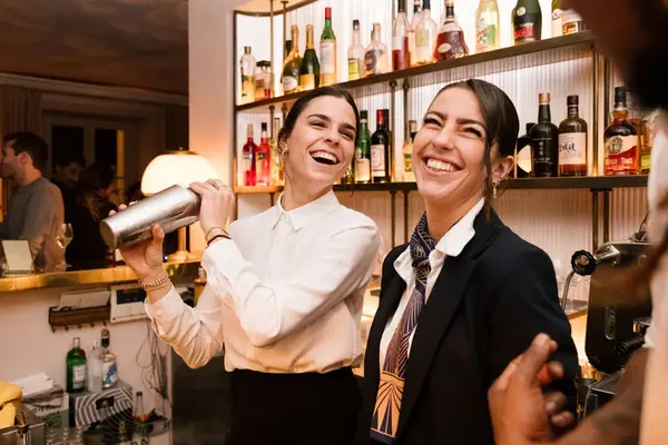 Reportage photo événementiel : deux barmaids souriantes préparent des cocktails au bar d'un hôtel particulier
