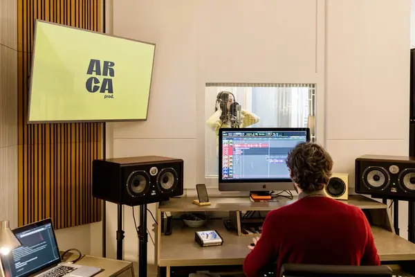 Reportage photo au studio Arca Productions à Paris : ingénieur du son à la console, comédienne en cabine derrière la vitre