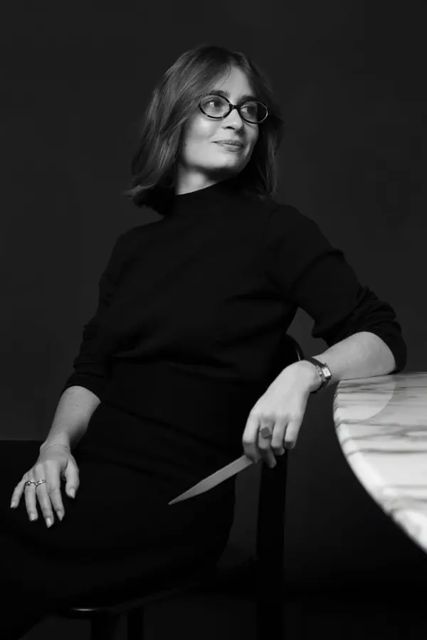 Portrait professionnel en noir et blanc de Mia, parfumeuse, assise près d'une table en marbre, une mouillette à la main