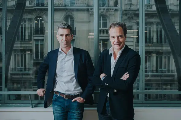 Portrait corporate de deux associés d'Alven debout devant une verrière ouverte sur des façades haussmanniennes à Paris