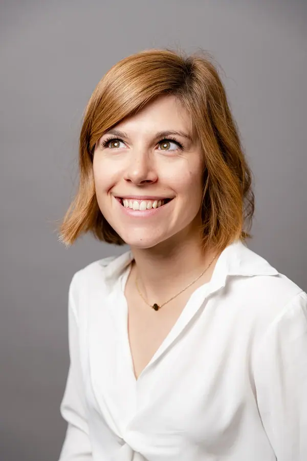 Portrait studio d'une collaboratrice souriante en chemise blanche sur fond gris, trombinoscope homogène