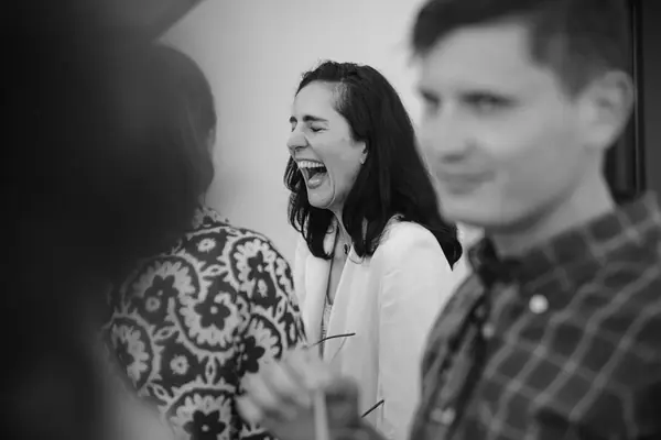 Reportage photo événementiel en noir et blanc : une invitée éclate de rire lors d'un événement d'entreprise, invités autour