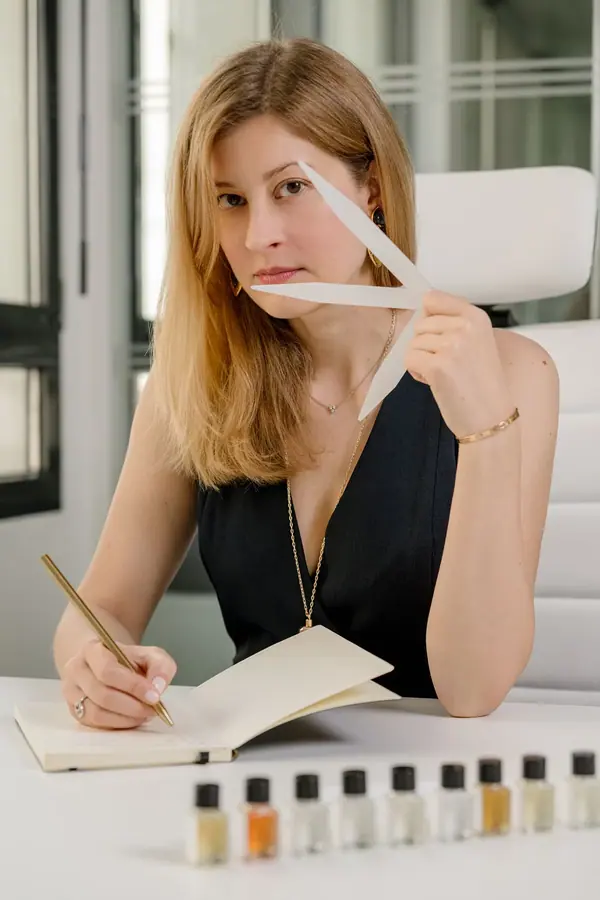 Portrait corporate de Claire à son bureau, touche à sentir à la main devant une rangée de flacons