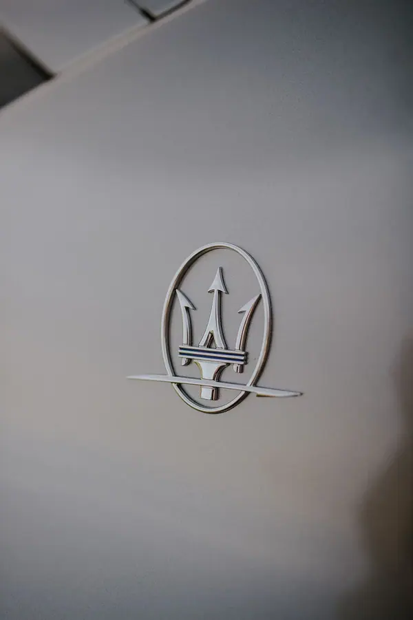 Gros plan sur le logo trident Maserati sur une carrosserie grise, reportage photo de détails automobiles