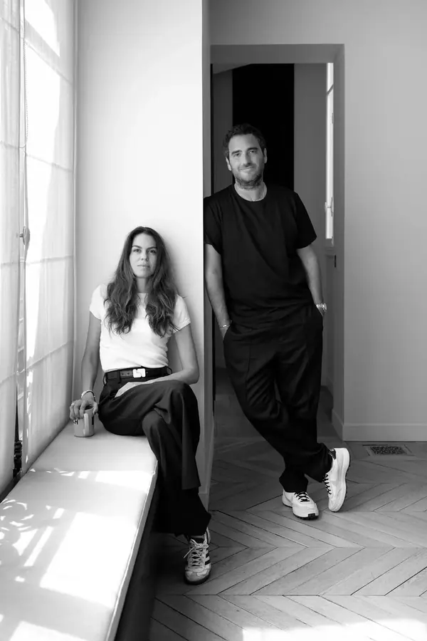 Portrait professionnel d'un duo dans un appartement lumineux, lui assis sur une banquette, elle debout sur un parquet
