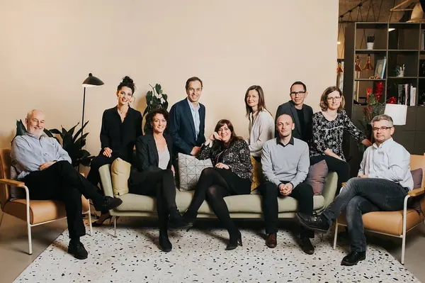 Portrait corporate de groupe de l'équipe Webloyalty, onze personnes réunies autour d'un canapé dans un salon lumineux