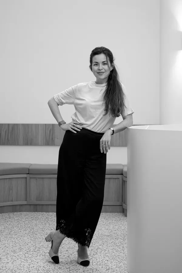 Portrait professionnel en noir et blanc d'une ophtalmologue debout, appuyée contre un comptoir, dans un cabinet lumineux