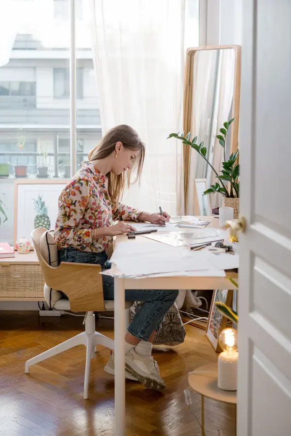 Portrait professionnel d'une femme dessinant à sa table de travail, près d'une fenêtre, dans un intérieur parisien lumineux