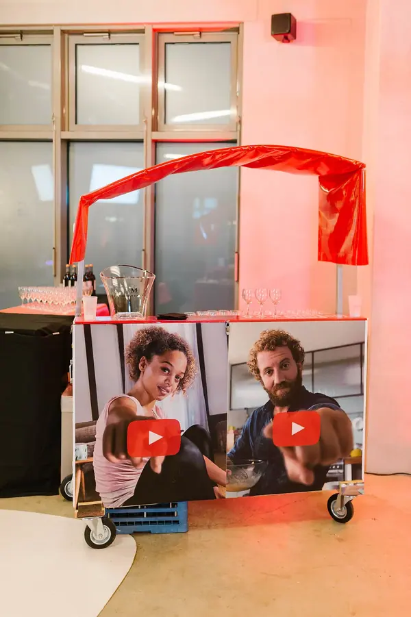 Reportage photo événementiel YouTube : chariot aux couleurs de la marque avec visuels vidéo, sous des lumières roses