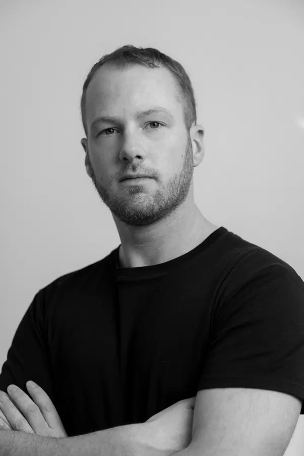 Portrait corporate noir et blanc d'un homme en veste sombre marchant sur une passerelle devant des immeubles modernes